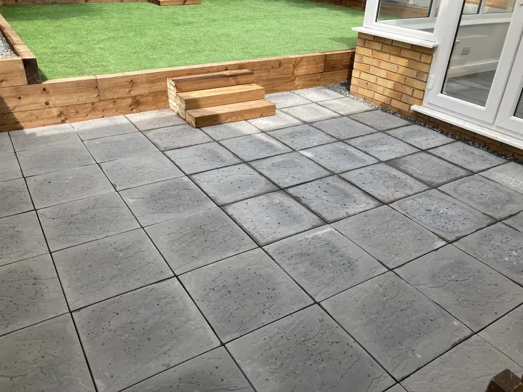 Grey slab patio with a timber sleeper raised lawn and steps